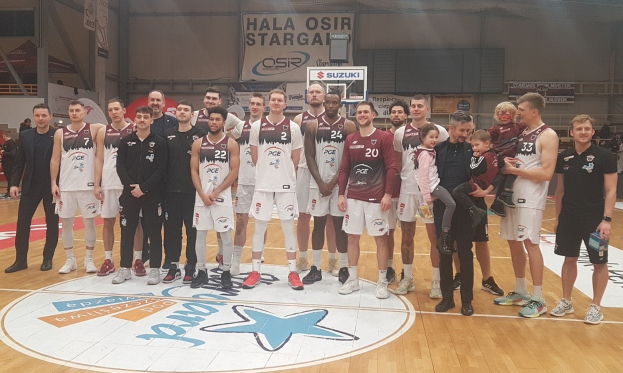 Männer- und Kindergruppe auf einem Basketballfeld mit Schildern "Hala Osir Starga" und Zuschauern im Hintergrund.