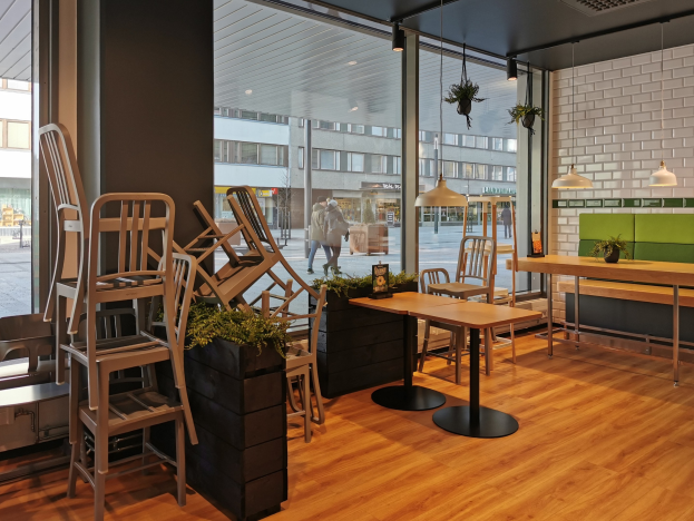 Innenansicht eines Restaurants in Berlin mit Holztischen und -stühlen in der Nähe eines großen Fensters, das auf eine Straße mit Fußgängern, Gebäuden und städtischen Elementen hinausgeht.