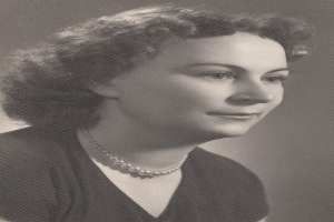 Ein Schwarz-Weiß-Foto einer Frau mit ernstem Gesichtsausdruck, deren Haar zurückgebunden ist und die eine Kette und ein einfaches Kleid mit hohem Kragen und langen Ärmeln trägt.