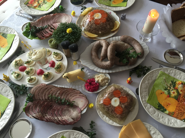 Ein langer Tisch mit verschiedenen Gerichten, Besteck, Gläsern und Kerzen, umgeben von Stühlen, der ein traditionelles deutsches Osteressen anzeigt.