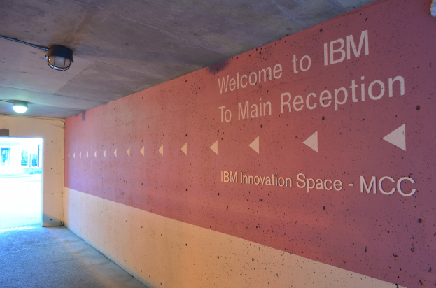 Wand mit beleuchteter Schrift 'Willkommen bei IBM' und einer Tür im Hintergrund, die in den IBM Innovation Space MCC führt.