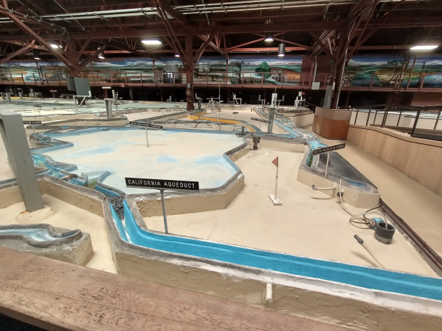 Großes Indoor-Wasserpark mit mehreren Wasserrutschen, Deckenbeleuchtung, Wandgemälden und einem Minigolfplatz mit Beschilderung.