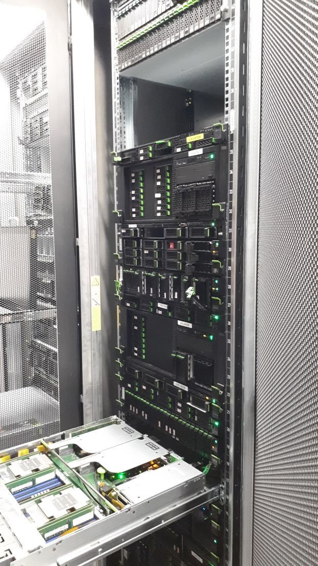 Server-Rack in einem Server-Raum mit elektronischen Geräten wie Switches und Routern, einem metallischen Objekt unten und einer Decke darüber.