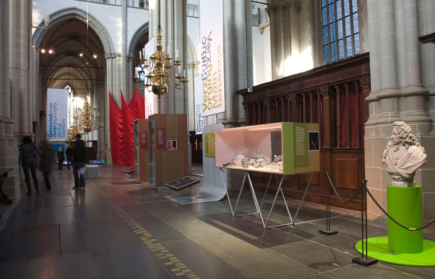 Ein geräumiger Museumsraum mit verschiedenen Ausstellungsstücken, darunter eine Statue auf einem Sockel, steht mit Seilen, textbehafteten Bannern, Säulen und Kronleuchtern, mit einigen Besuchern.