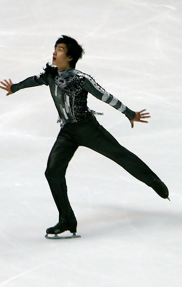 Mann in schwarzer Eiskunstlaufbekleidung gleitet über eine Eisfläche und führt eine Choreographie aus.