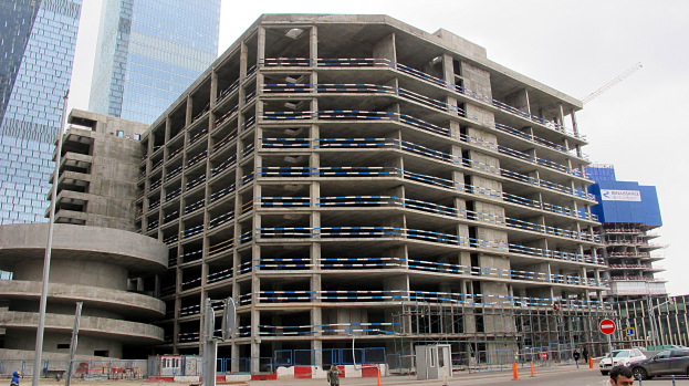 Großes Bauprojekt in einer Stadt mit Wolkenkratzern, Fahrzeugen, Passanten, Verkehrsinfrastruktur und Kränen vor einem klaren Himmel.