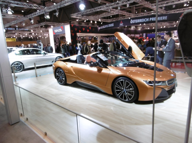 Ein elegantes schwarzes BMW i8 Cabrio mit Chromakzenten auf der IAA in Frankfurt umgeben von formell gekleideten Besuchern in einer Atmosphäre der Aufregung.