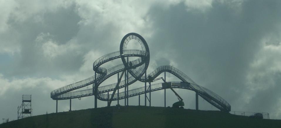 Eine Achterbahn auf dem Höhepunkt eines Hügels unter einem bewölkten Himmel, mit sichtbaren Stützpfählen und -strukturen.