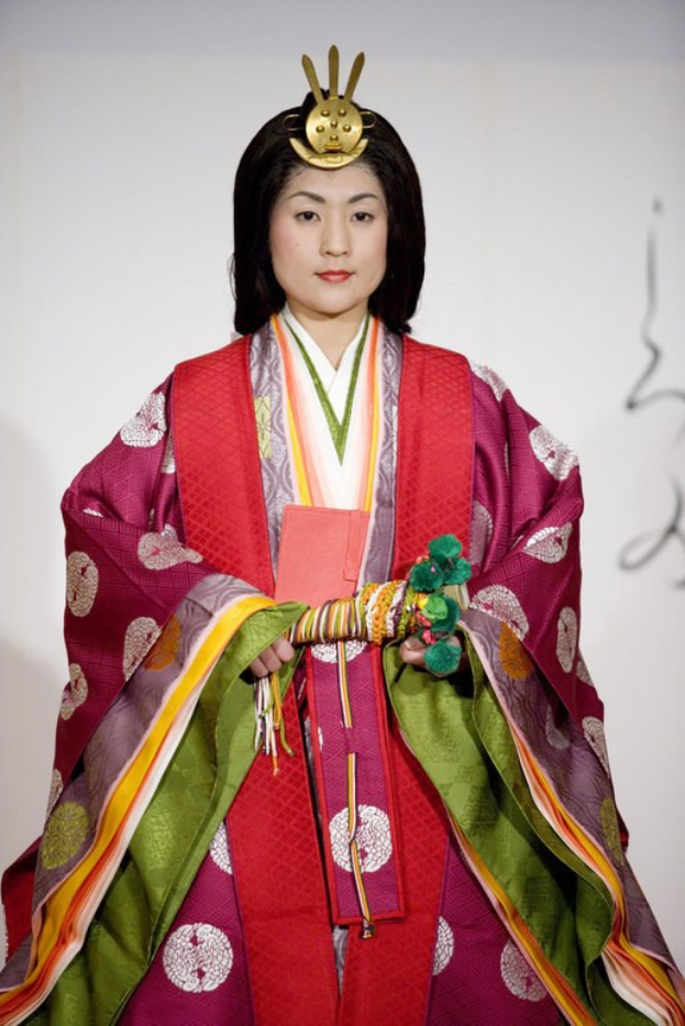 Eine Frau in einem traditionellen japanischen Kimono steht selbstbewusst auf einem Laufsteg, trägt ein leuchtend rotes und grünes Kleid mit detaillierten Mustern, ihr Haar ist ordentlich zu einem Knoten gebunden.