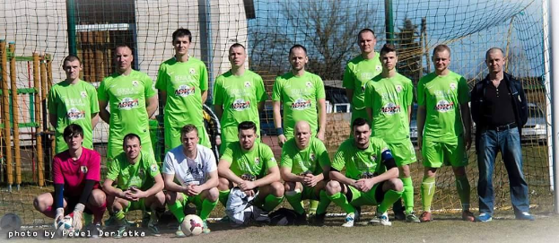 Eine Gruppe von Männern in grünen T-Shirts steht auf einem Fußballfeld, einige hocken, mit einem Ball davor und einem Torpfosten rechts daneben.