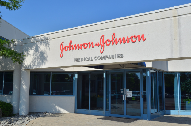 Außenansicht des Johnson & Johnson Medical Companies-Gebäudes mit Glaswänden, Text an der Wand, Steinen, Pflanzen und einem Baum auf der linken Seite, unter einem klaren blauen Himmel.