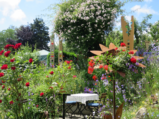 Ein Garten mit bunten Blumen und Pflanzen, mit einem Tisch mit einer Decke und Stühlen in der Mitte, umgeben von Bäumen unter einem bewölkten Himmel auf dem Chelsea Flower Show.