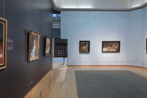 Ein prächtiger Raum in der Nationalgalerie in London, gefüllt mit zahlreichen Gemälden an den Wänden, einem Teppichboden, Geländern und einer Decke mit Beleuchtung.