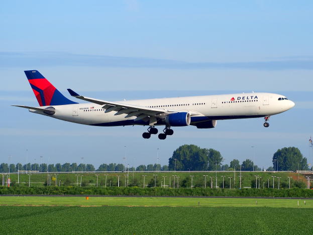Delta Air Lines Boeing 787-9 Dreamliner beim Start vom Frankfurt Airport, grünes Gras unten, Lichtmasten und Bäume im Hintergrund, Kontrollturm rechts, weiße Wolken am Himmel.