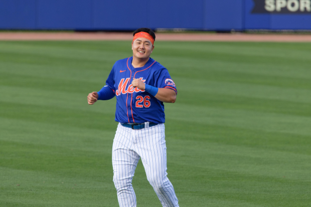 Ein Baseballspieler in einem blauen T-Shirt, weißen Hosen und einem orangen Stirnband rennt über ein Feld und strahlt dabei übers ganze Gesicht, während im Hintergrund eine blaue Tafel mit Text zu sehen ist.