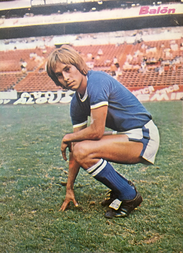 Ein Mann kniet auf einem Fußballfeld umgeben von Menschen auf Stühlen und Tafeln mit Text.