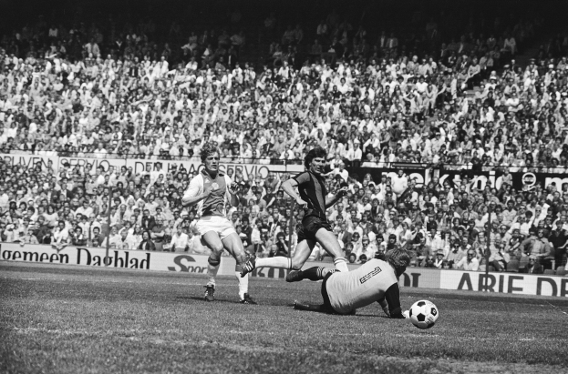 Schwarzes und weißes Foto von Männern, die auf einem Feld Füßball spielen, mit Zuschauern im Hintergrund und einem Banner 'Bundesliga 1978-79 Ajax 1-1 Hannover 96'.