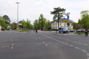 Eine Kreisverkehrausfahrt mit einem parkenden Polizeiauto, Fahrzeugen auf der Straße, Fußgängern auf dem Gehweg, Verkehrsampeln, Gebäuden, Bäumen und einem bewölkten Himmel.