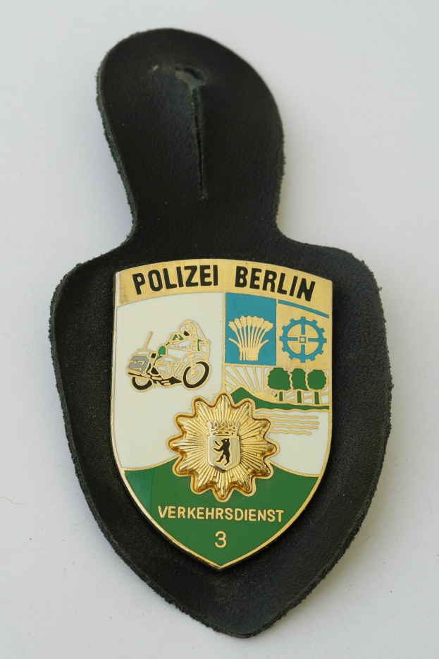 Ein schildförmiges Polizeisiegel mit der Aufschrift "Polizei Berlin" auf blauem Hintergrund, weißem Rand, weißem zentralen Stern und schwarzer fetter Schrift, das auf einer Oberfläche liegt.