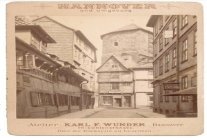 Ein altes Foto einer Straße in Hannover, Deutschland, mit Gebäuden auf beiden Seiten und Text oben und unten.