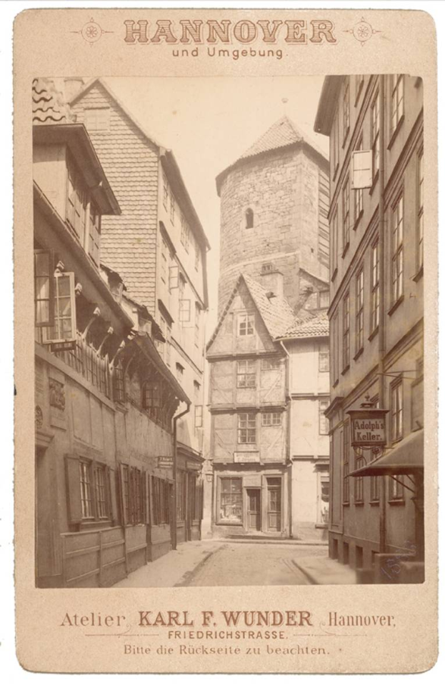 Ein altes Foto einer Straße in Hannover, Deutschland, mit Gebäuden auf beiden Seiten und Text oben und unten.