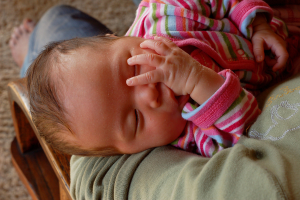 Eine Person sitzt und hält ein schlafendes Kind, mit einer Matte am unteren Bildrand.