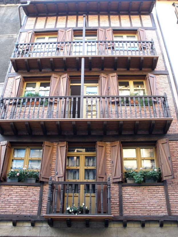 Altes Gebäude mit mehreren Fenstern, Balkonen, Geländern, Türen und Blumentöpfen mit Pflanzen in Straßburg, Frankreich.