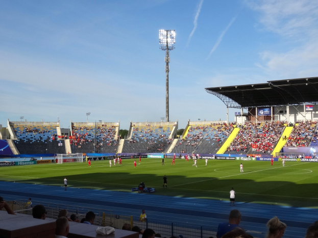 Ein Fußballspiel in einem großen Stadion mit Spielern auf dem Feld und Zuschauern in den Rängen unter Flutlicht.