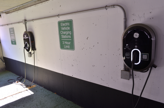 Eine Elektrofahrzeug-Ladestation in einer Tiefgarage mit zwei an der Wand angebrachten Ladepunkten und Tafeln mit Text darauf, der Boden ist unten im Bild zu sehen.
