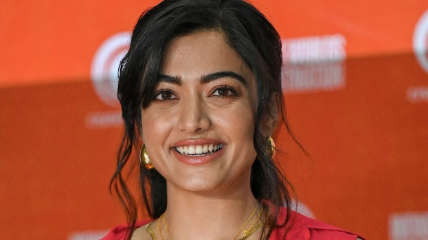 Eine Frau in einem leuchtend roten Kleid mit einem eleganten Dutt und dezentem Make-up steht strahlend da, trägt schwarze High Heels und hat einen hellgelben Banner mit der Aufschrift "Sonam Kapoors beste Schönheits Looks vom Cannes Film Festival" im Hintergrund.