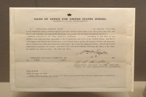 Ein Blatt mit dem Text "Eid des Bundesrichters der Vereinigten Staaten" darauf, das auf einem Tisch vor einer Wand liegt.