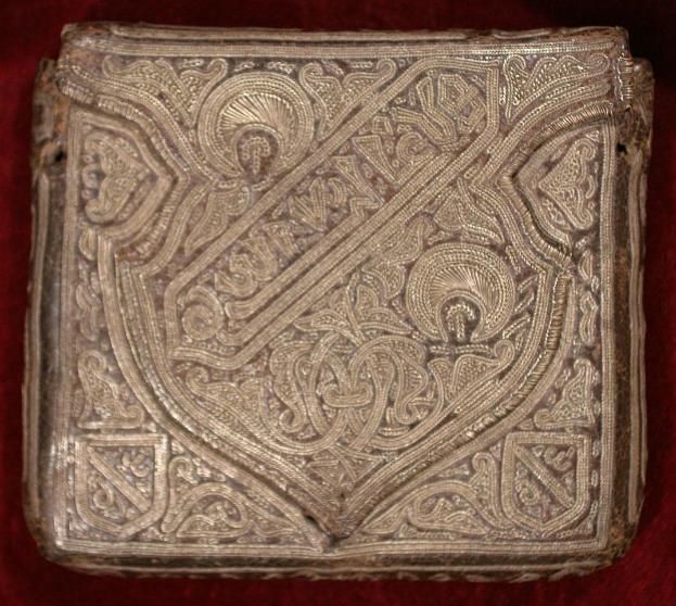 Altes Buch mit goldener Hülle, das auf einem roten Samtgrund mit kunstvollen Verzierungen prunkt.