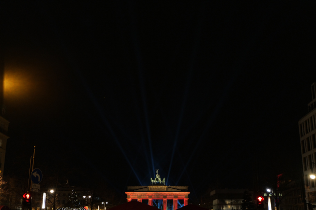 Das Brandenburger Tor bei Nacht, beleuchtet von Straßenlaternen, mit umliegenden Gebäuden, Bäumen, Pfählen, Verkehrszeichen, Schildern und Zelten gegen einen dunklen Himmel.