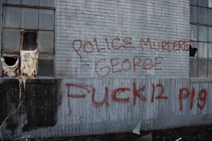 Ein Gebäude mit Graffiti, das "Polizei ermordet George Fuck 12 P19" auf der Seite trägt, mit Fenstern und verschiedenen Gegenständen vorne auf dem Boden.