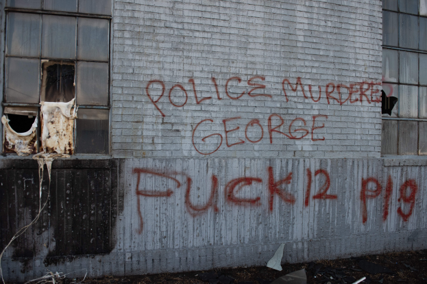 Ein Gebäude mit Graffiti, das "Polizei ermordet George Fuck 12 P19" auf der Seite trägt, mit Fenstern und verschiedenen Gegenständen vorne auf dem Boden.