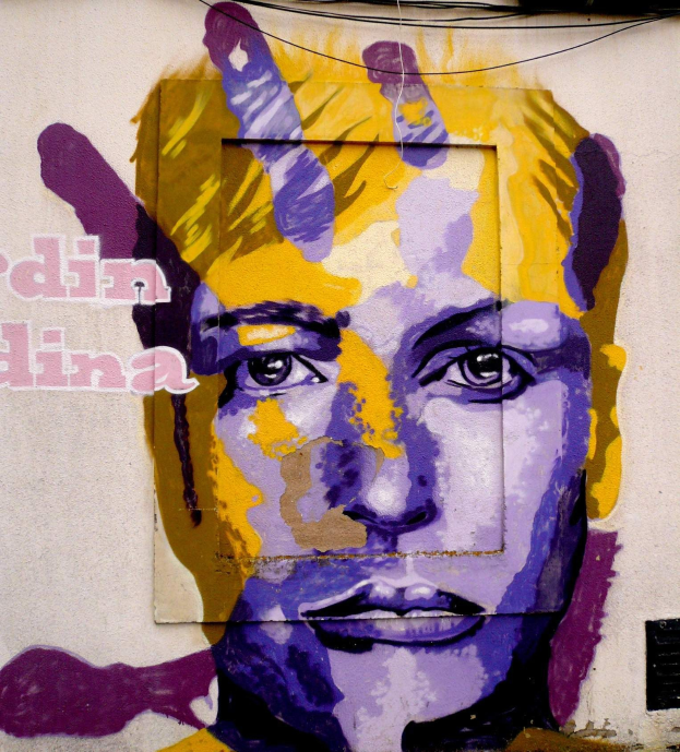 Ein leuchtendes, farbenfrohes Wandbild eines Frauenkopfs auf einem Berliner Gebäude, das detaillierte Merkmale und großen Text auf der Wand zeigt.