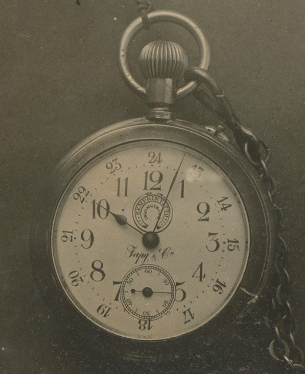 Ein Schwarz-Weiß-Foto einer antiken Taschenuhr mit einer Kette, das eine nummerierte Zifferblat zeigt.