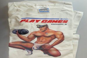 Ein weißes T-Shirt mit einem Motiv eines entschlossenen Mannes in einem blauen Hemd, der eine Hantel hält, und der Text 'Spiele' in fetten schwarzen Buchstaben.