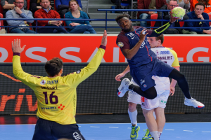 Eine Gruppe von Männern, die auf einem Platz Handball spielen, mit einem Ball in der Luft und Zuschauern im Hintergrund, die das Spiel beobachten, mit einem Schild, auf dem "Futsal-Weltmeisterschaft 2019 - Paris Saint-Germain vs Bordeaux" steht.