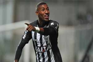 Fußballspieler in einem schwarz-weißen gestreiften Trikot, der ein Tor feiert und lächelt, Hintergrund unscharf.