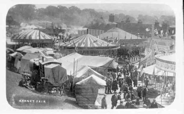 Schwarzes und weißes Foto eines Karnevals mit Zelten, Menschen, Wagen, Pfosten, Bäumen und Gebäuden, beschriftet mit 'Barnet Fair, London, England'.