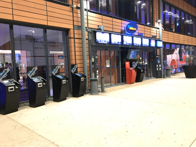 Großer Raum mit mehreren wandmontierten Fernsehern, die ein Sportwetten-System anzeigen, Glasfenster, Deckenbeleuchtung und zusätzliche Ausstattung.