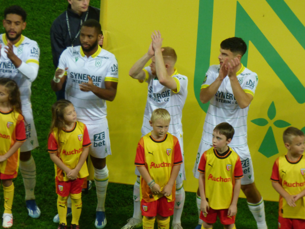 Gruppe von Fußballspielern in Uniformen, die auf einem Feld mit einem "Ligue 1"-Schild im Hintergrund klatschen und einen Sieg feiern.
