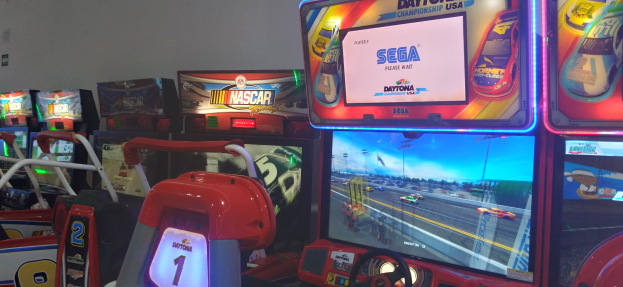 Eine Reihe von buntfarbenen Arcade-Rennwagenautomaten in einem Raum mit einer Wand im Hintergrund.