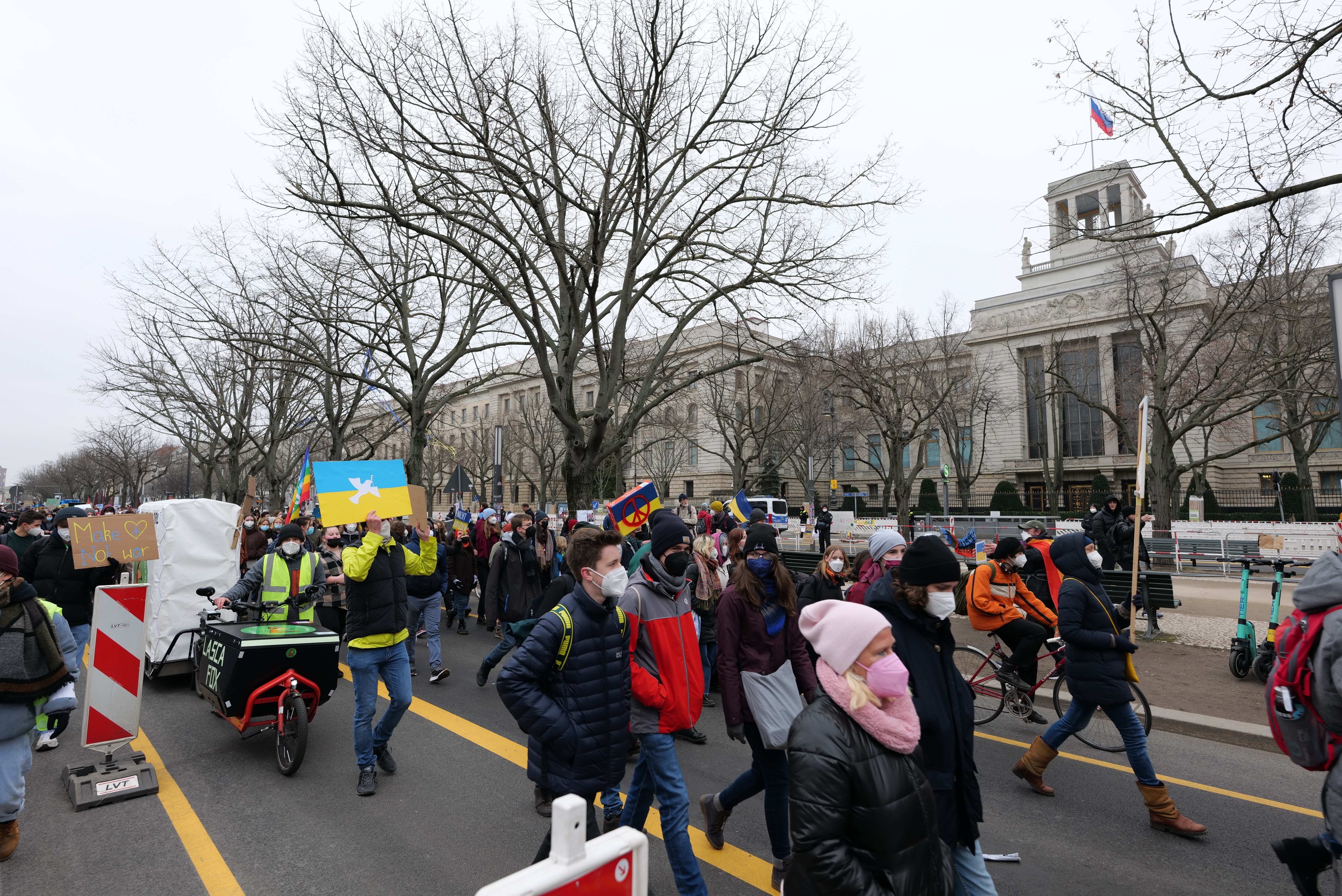 Eine große Gruppe von Menschen marschiert auf einer Demonstration in Washington, D.C. mit Schildern und Transparenten, während einige Fahrräder fahren, unter einem klaren blauen Himmel.