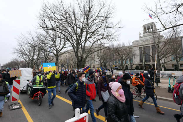 Eine große Gruppe von Menschen marschiert auf einer Demonstration in Washington, D.C. mit Schildern und Transparenten, während einige Fahrräder fahren, unter einem klaren blauen Himmel.
