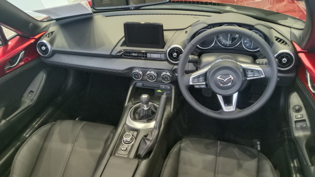 Das Innere eines roten Mazda MX-5 Miata RF mit schwarzen Ledersitzen, Lenkrad, Gangschaltung, Knöpfen, Bildschirm und Rückspiegel.