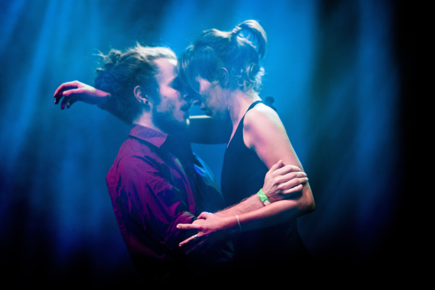 Zwei Menschen umarmen und küssen sich auf einer Bühne mit Hintergrundbeleuchtung.