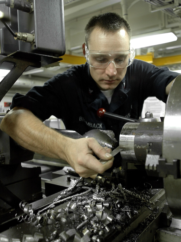 Ein Monteur mit Schutzbrille bedient eine Maschine in einer hell erleuchteten Fabrikumgebung.