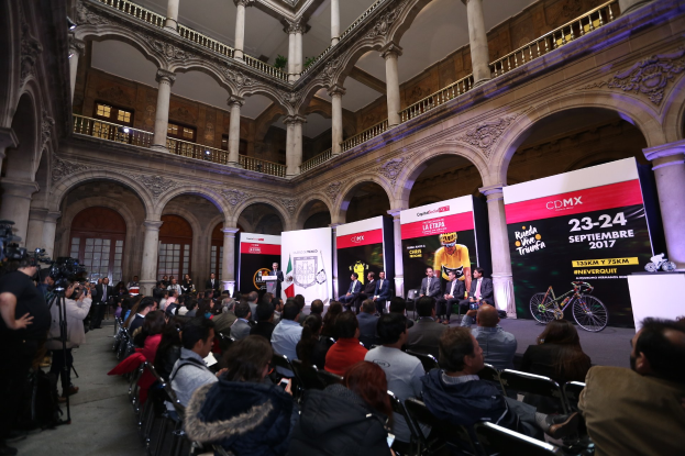 Eine Gruppe von Menschen an einem Tisch mit Mikrofon und Rednerpult vor einer Menge, Kameras und Transparenten, was eine Pressekonferenz für das CDMX 2017-Event vermuten lässt.